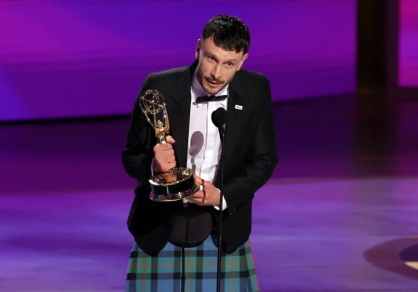 Richard Gadd speaks into a microphone as he accepts an Emmy on stage