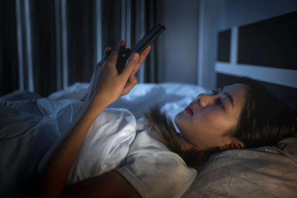 A woman using her mobile phone while lying on her bed at night